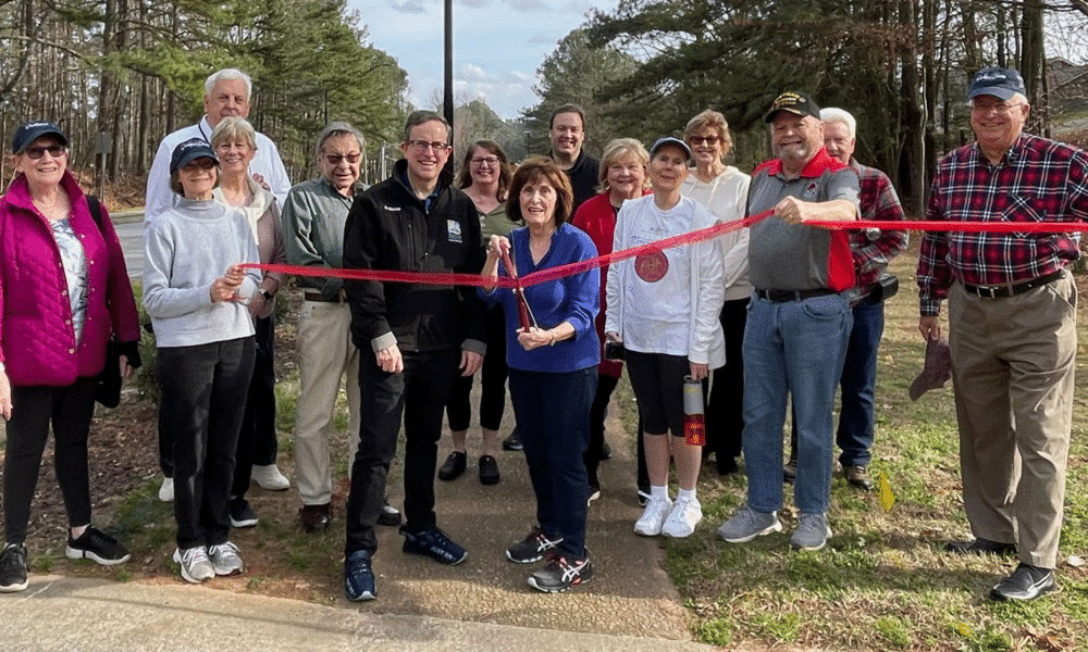 Susan Albright (with scissors) and Peachtree Corners Councilmember Eric Christ (in black jacket), along with Dunwoody Manor neighbors, ready to cut the ribbon with one of the new street lights in the background.