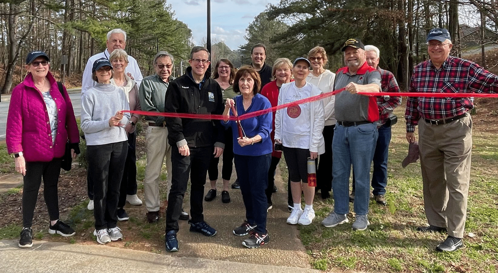 Susan Albright (with scissors) and Peachtree Corners Councilmember Eric Christ (in black jacket), along with Dunwoody Manor neighbors, ready to cut the ribbon with one of the new street lights in the background.