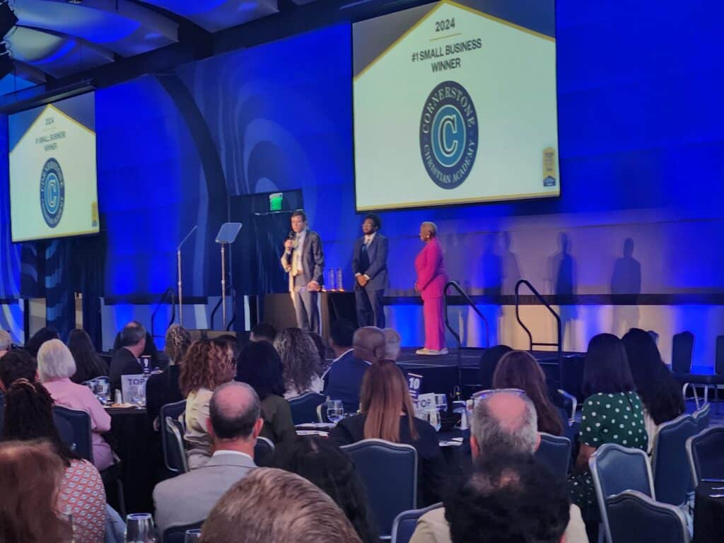 Three people on stage in front of an audience at an awards show honoring the #1 small business winner 2024