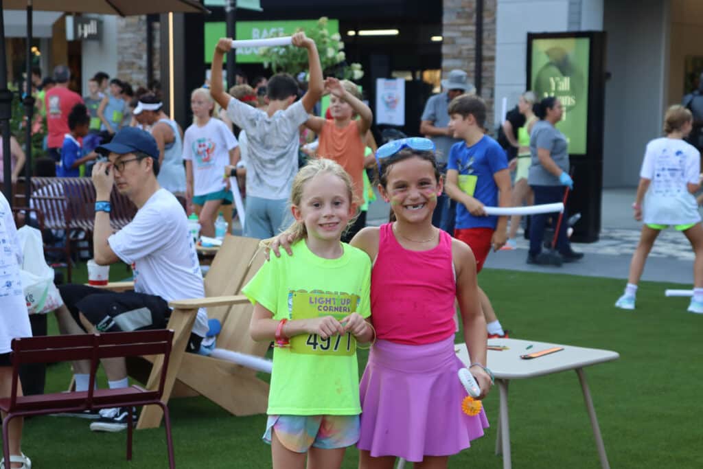 Two smiling young girls with faces painted at an outdoor public event