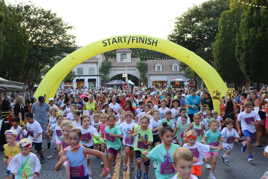 Large group of people running in a race with an inflatable start/finish race arch above them