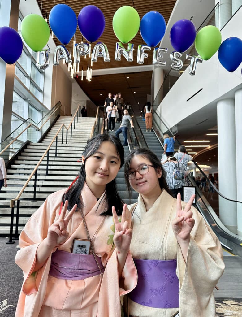 Two girls in kimonos standing under a Japanfest balloon banner