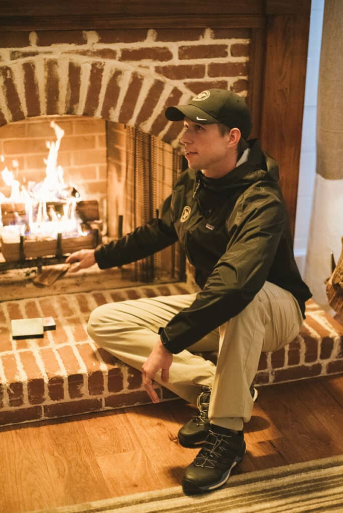 man in cap sitting in front of a fireplace