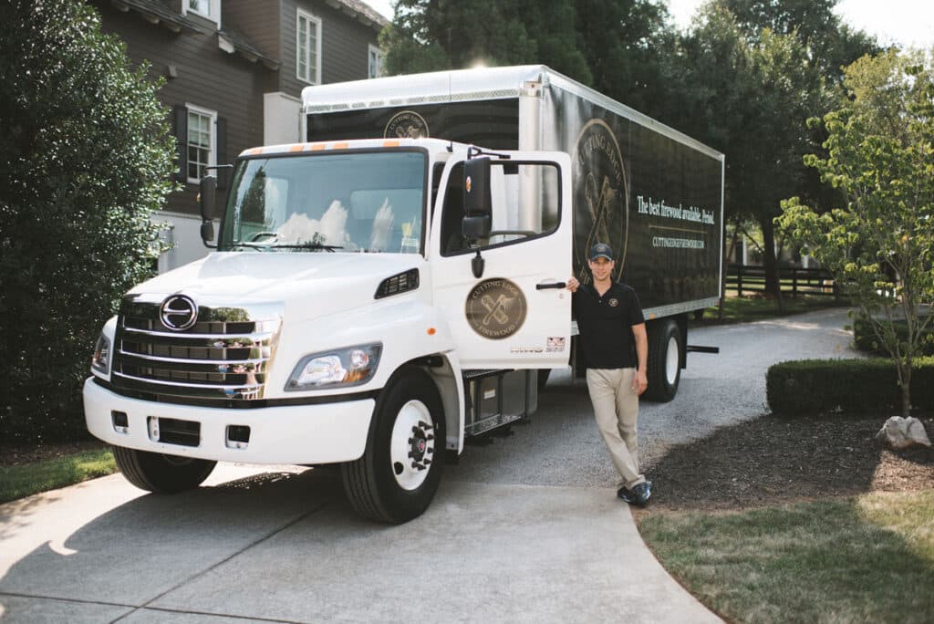 man standing next to firewood delivery truck