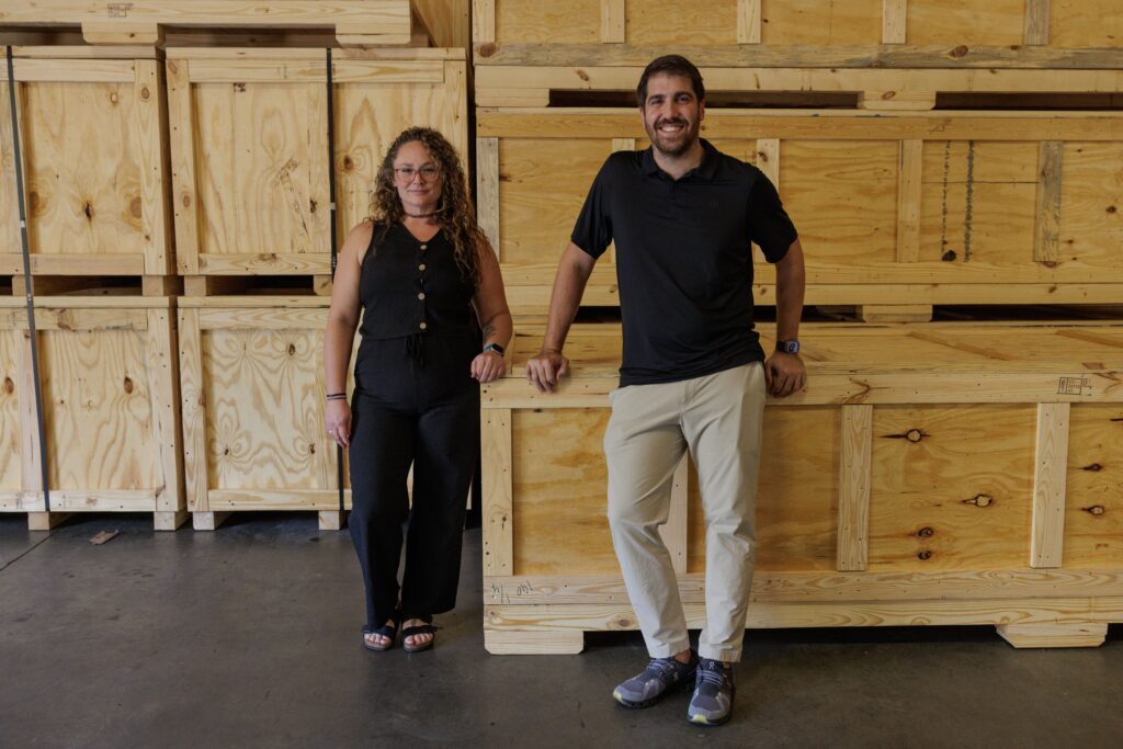 two people from TransPak standing in front of crates and boxes in a warehouse