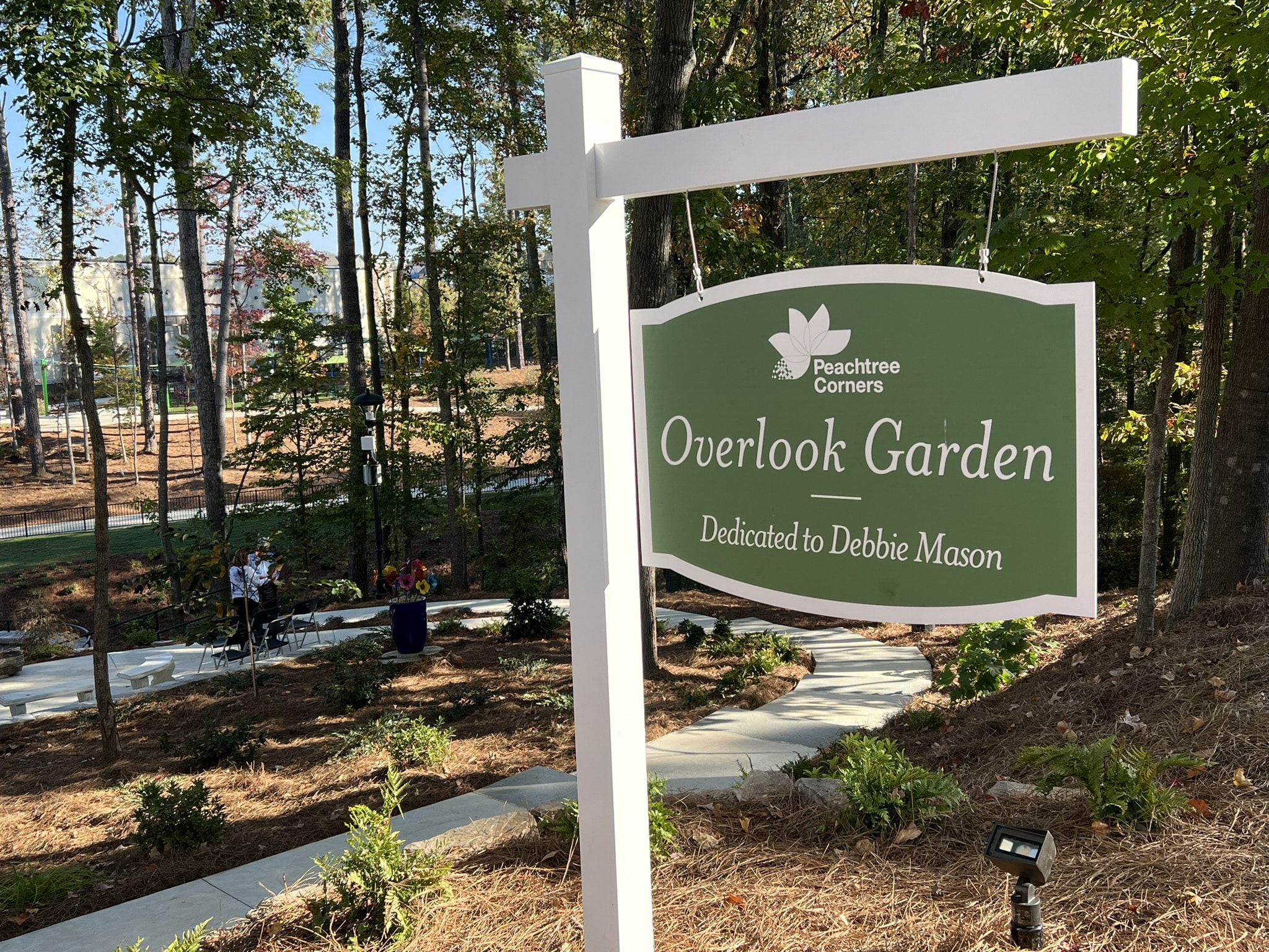 A green sign with white lettering and white post for the Debbie Mason Overlook Garden in Peachtree Corners