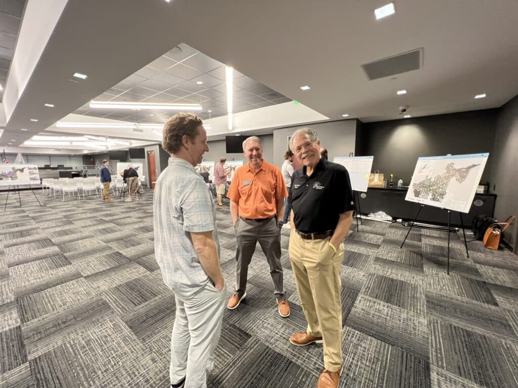 three men standing together in a spacious meeting room