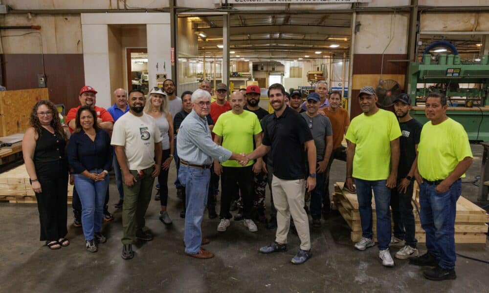 group of people in a warehouse with two men in front shaking hands