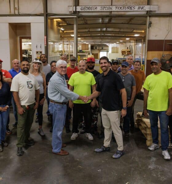 group of people in a warehouse with two men in front shaking hands