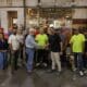 group of people in a warehouse with two men in front shaking hands