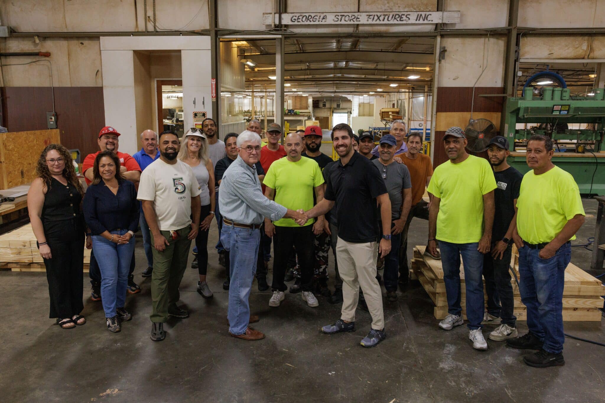 group of people in a warehouse with two men in front shaking hands