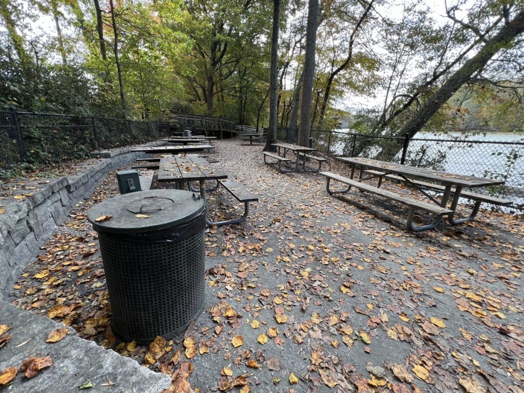 Picnic tables and trashcan by the river at Jones Bridge Park on a fall day