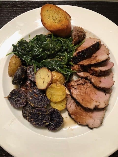 a plate of pork tenderloin with spinach and potatoes