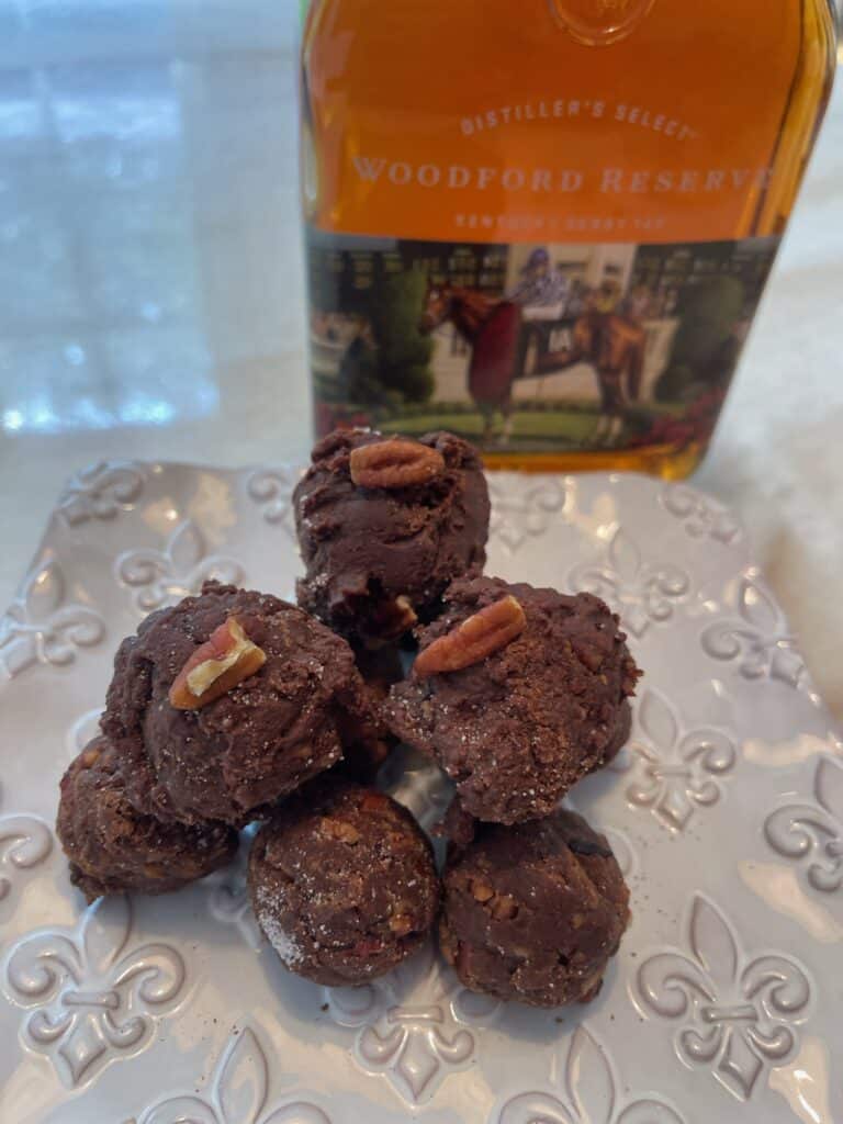 a small plate of Bourbon Balls next to a bottle of bourbon on a white kitchen counter