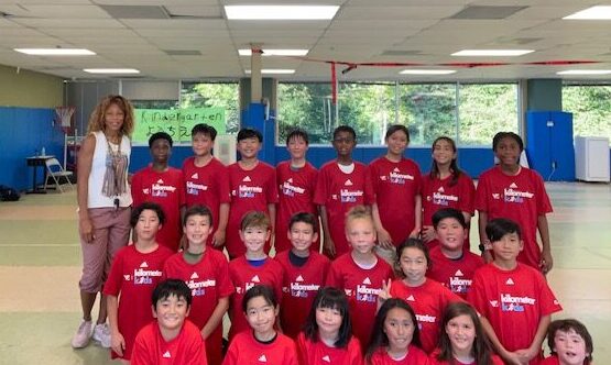 Group of young track students in red shirts, indoors in their gym space with their coach.