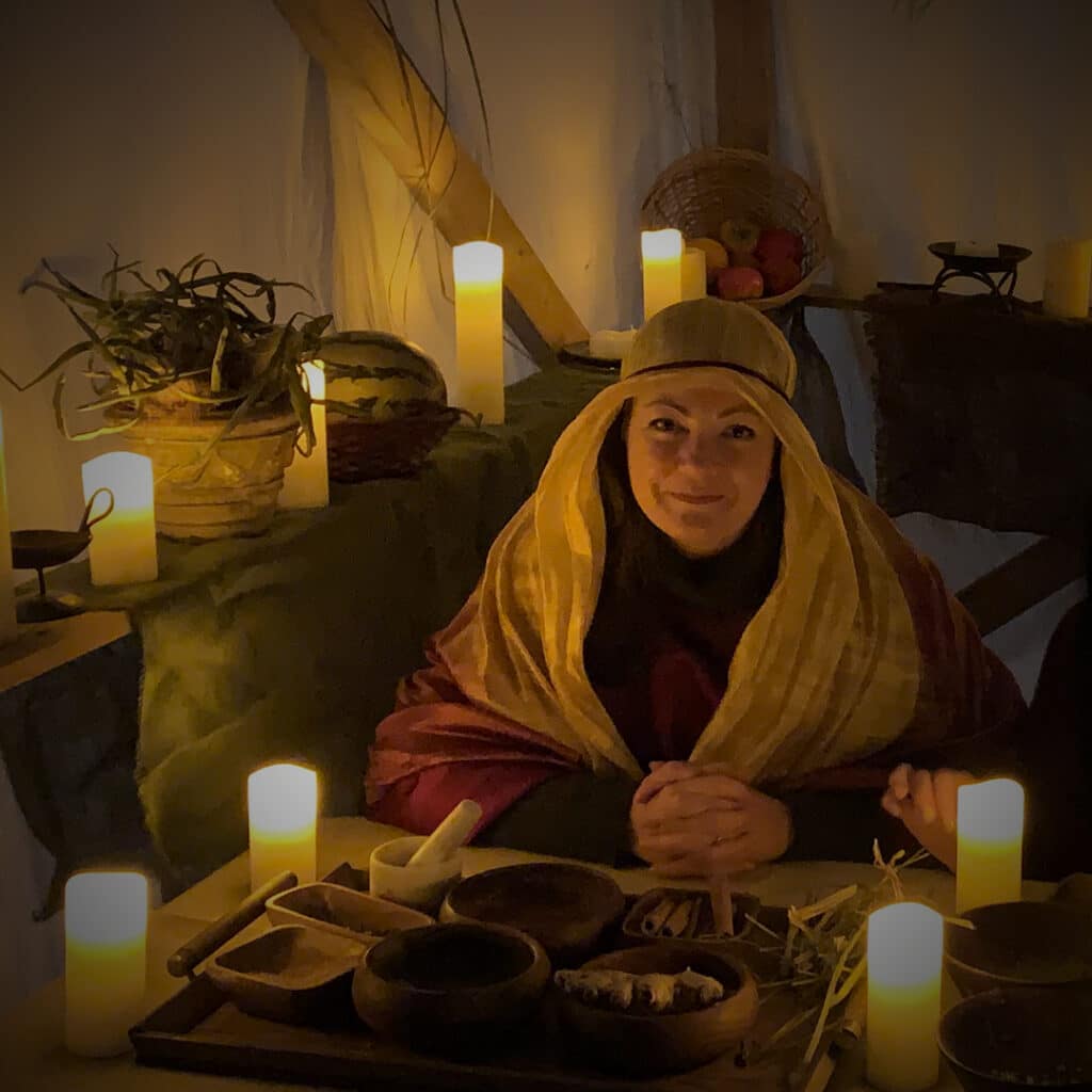 A woman dressed as a shopkeeper from old Bethlehem, surrounded by lit candles and items for sale