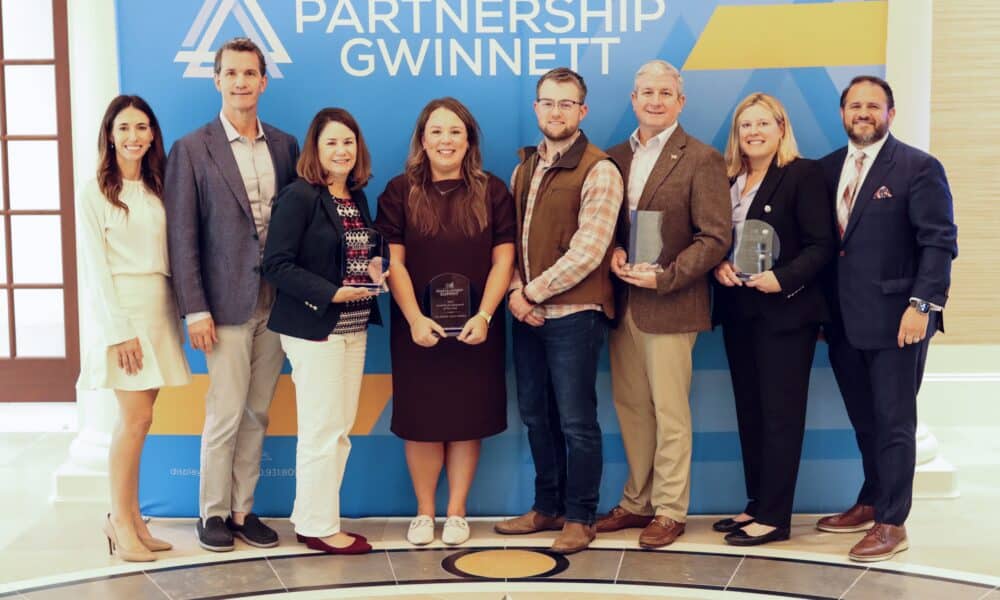 A group of award winners in front of a Partnership Gwinnett sign