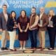 A group of award winners in front of a Partnership Gwinnett sign