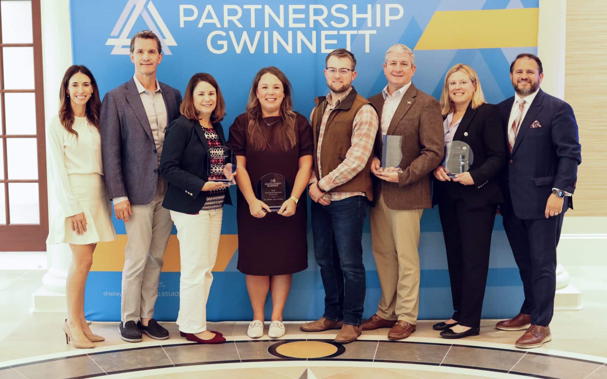 A group of award winners in front of a Partnership Gwinnett sign