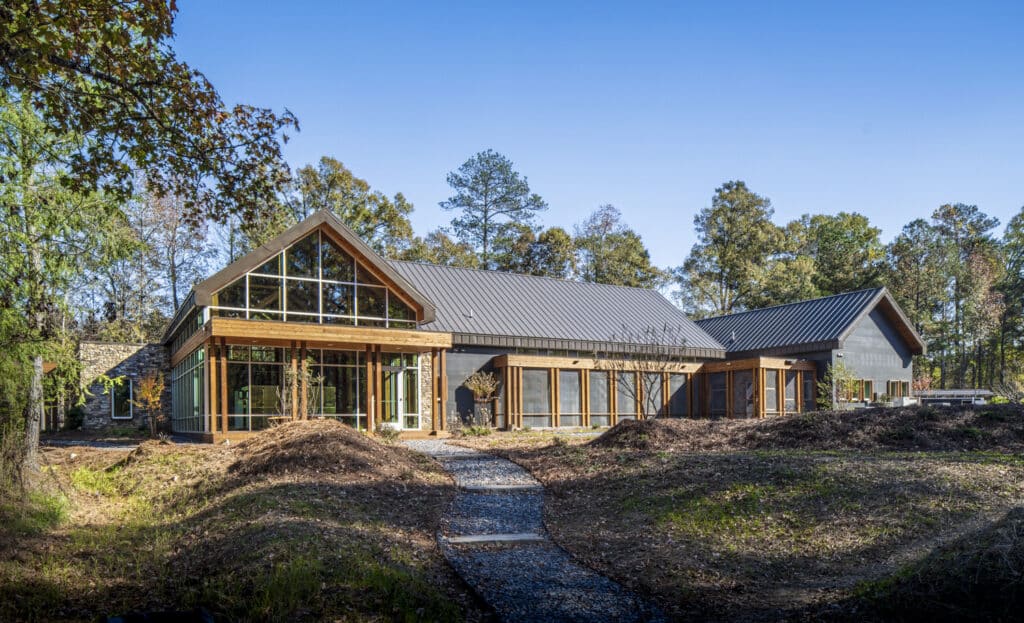 Wood-framed building with lots of windows set within a lightly wooded landscape