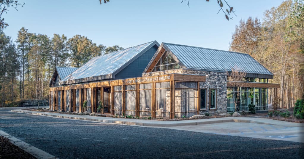 Full view of the award-winning cat shelter at Furkids. It's a wood-framed building with lots of windows, set within a lightly wooded landscape.