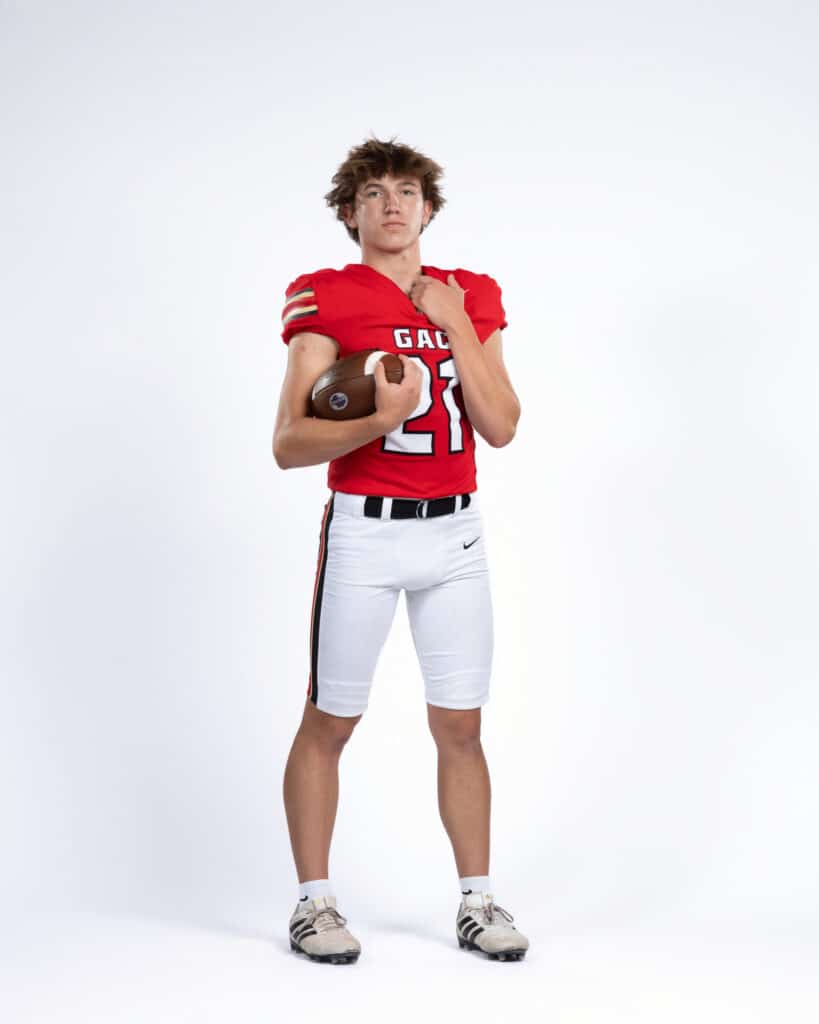 High School football player in a red and white uniform, holding a football and posing for a senior photo