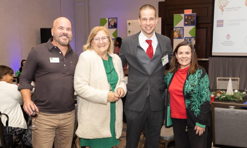 Two men and two women wearing name tags posing for a photo at an end-of-year business event