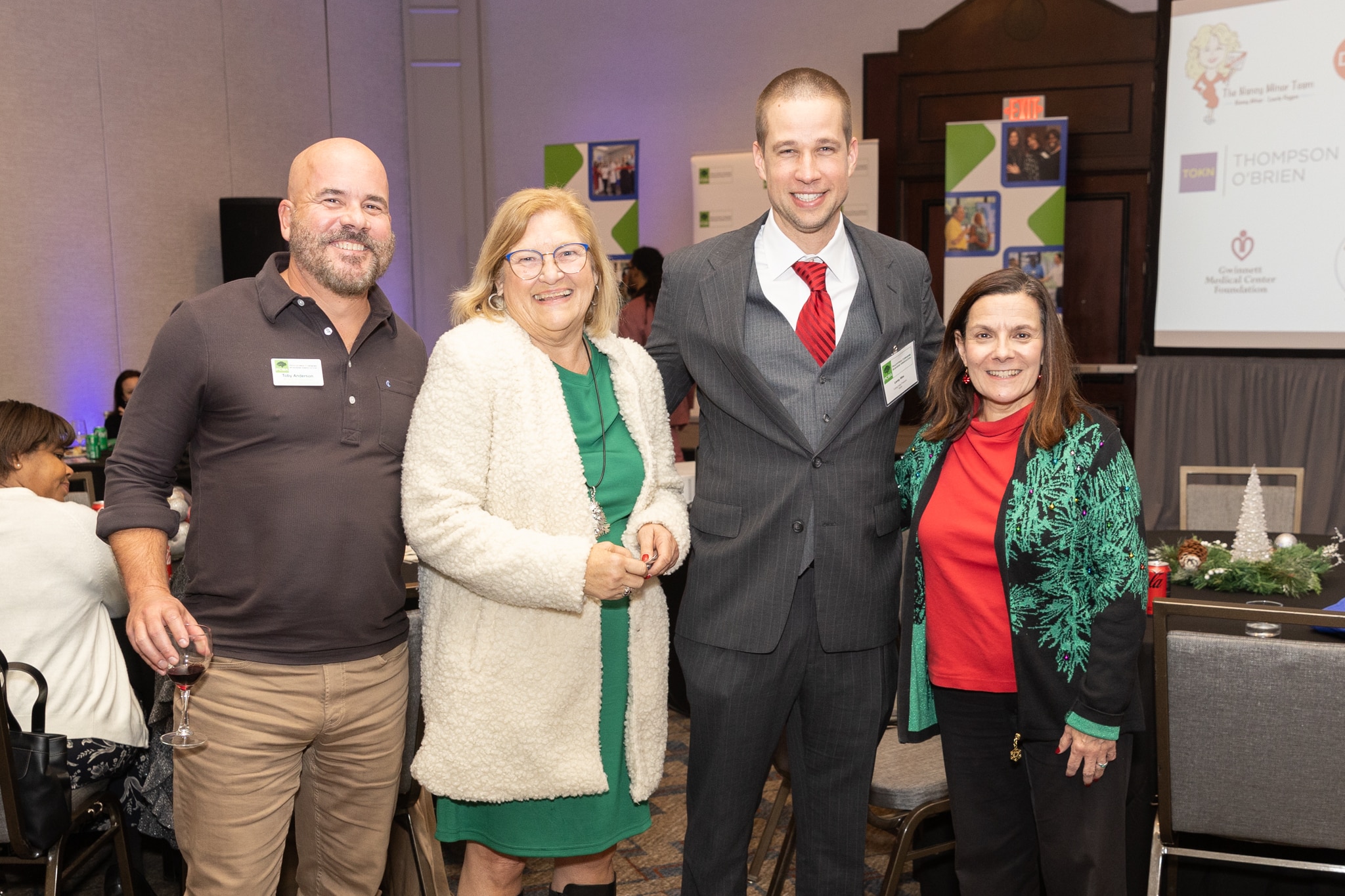 Two men and two women wearing name tags posing for a photo at an end-of-year business event