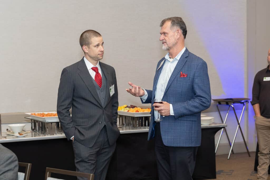 Two men in suits standing in front of a buffet table at a business event talking