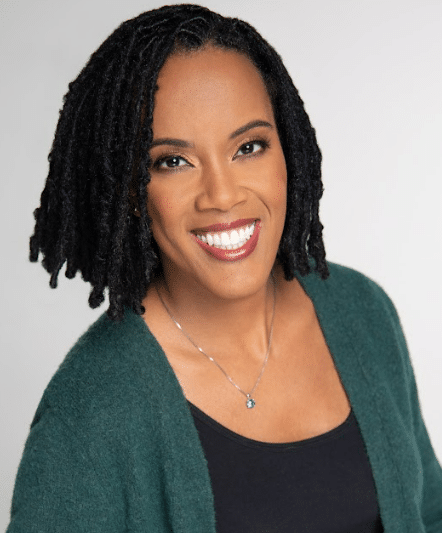 Head shot of author, Jill Tew. She's wearing a black top with green jacket over it, smiling and looking at the camera.