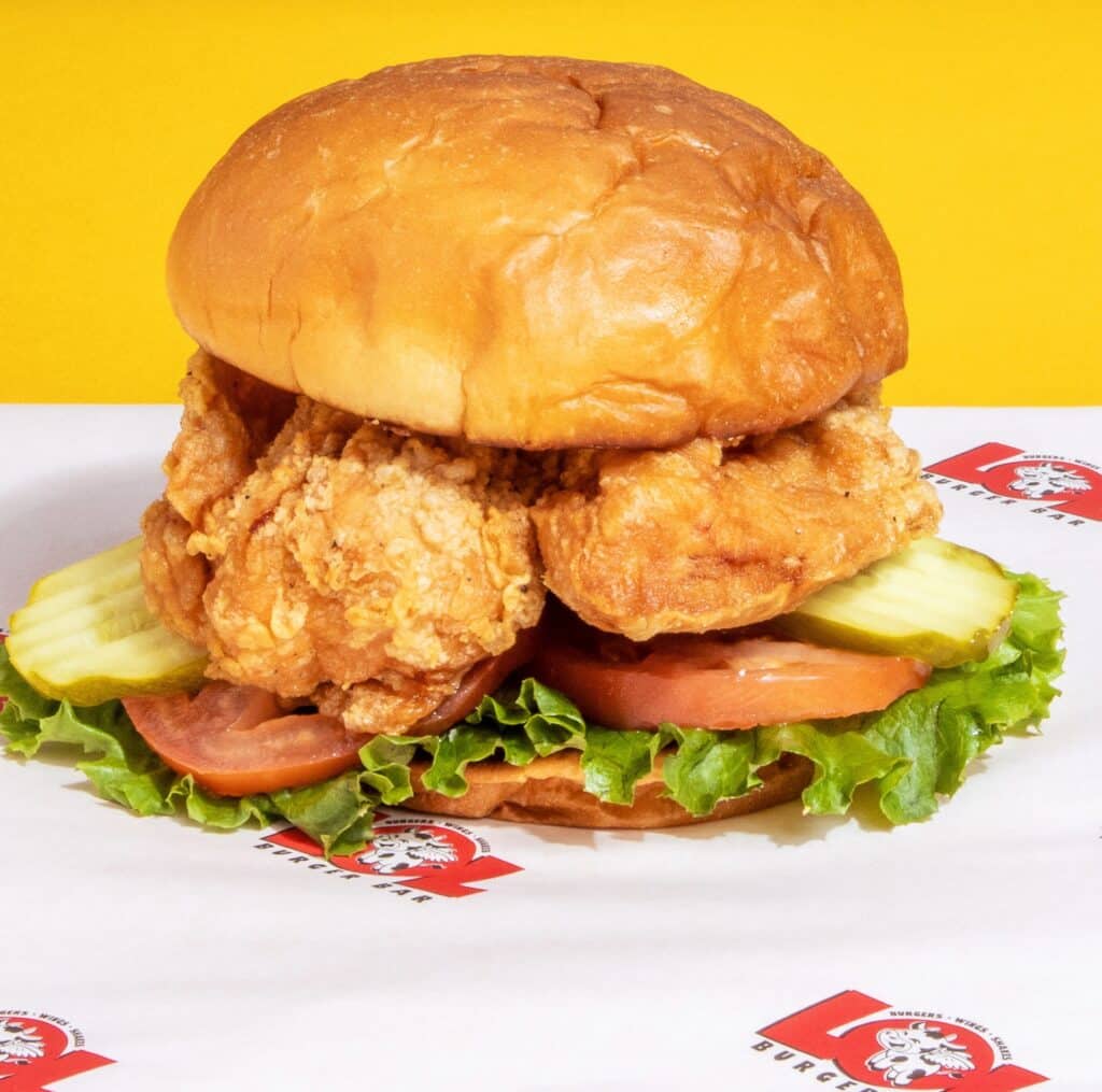 Fried chicken sandwich on a bun with lettuce and pickles. Set against a yellow background