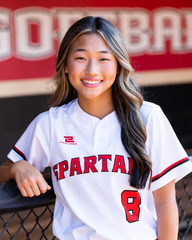 High school girl with long brown hair wearing a red and white Spartans jersey