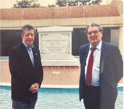 Two men standing in front of a small monument and fountain