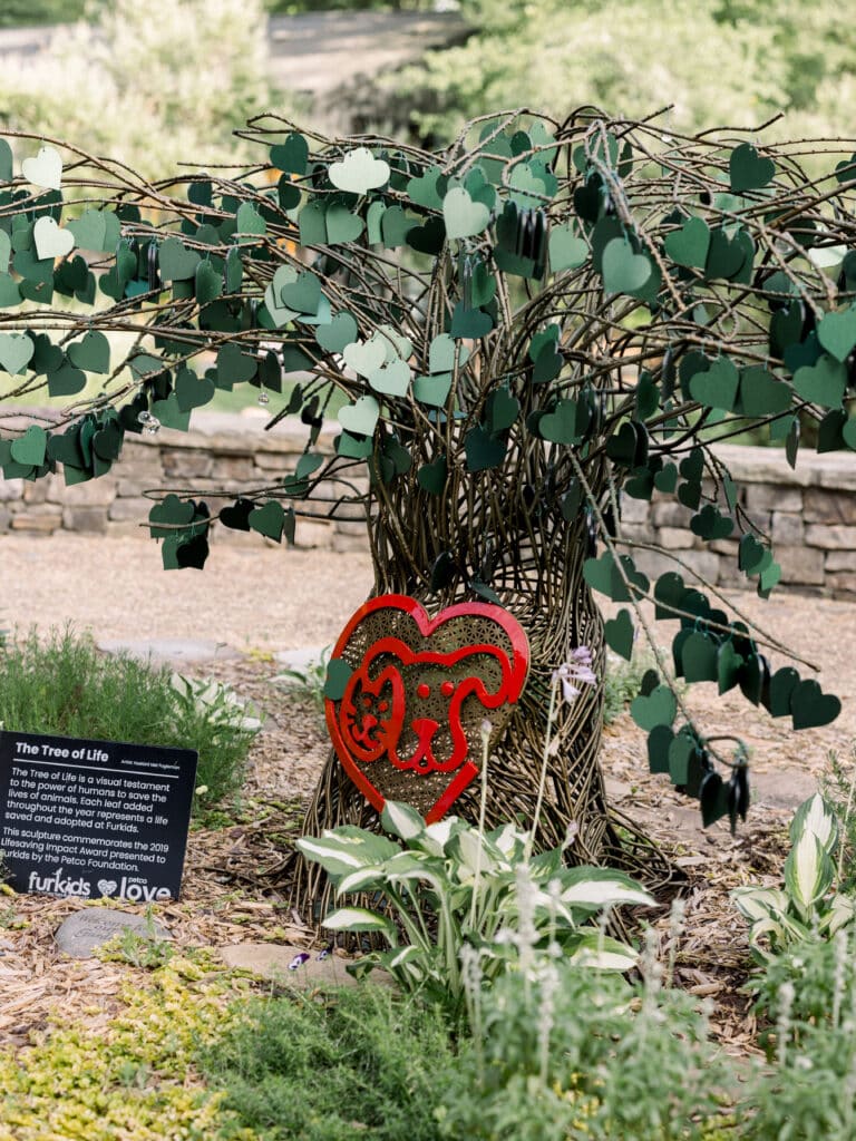 Small  'tree of life' sculpture outdoors at Furkids' headquarter campus. There's a red dog/cat/heart logo on the tree and a plaque beside it to commemorate the organization's Lifesaving Impact Award.