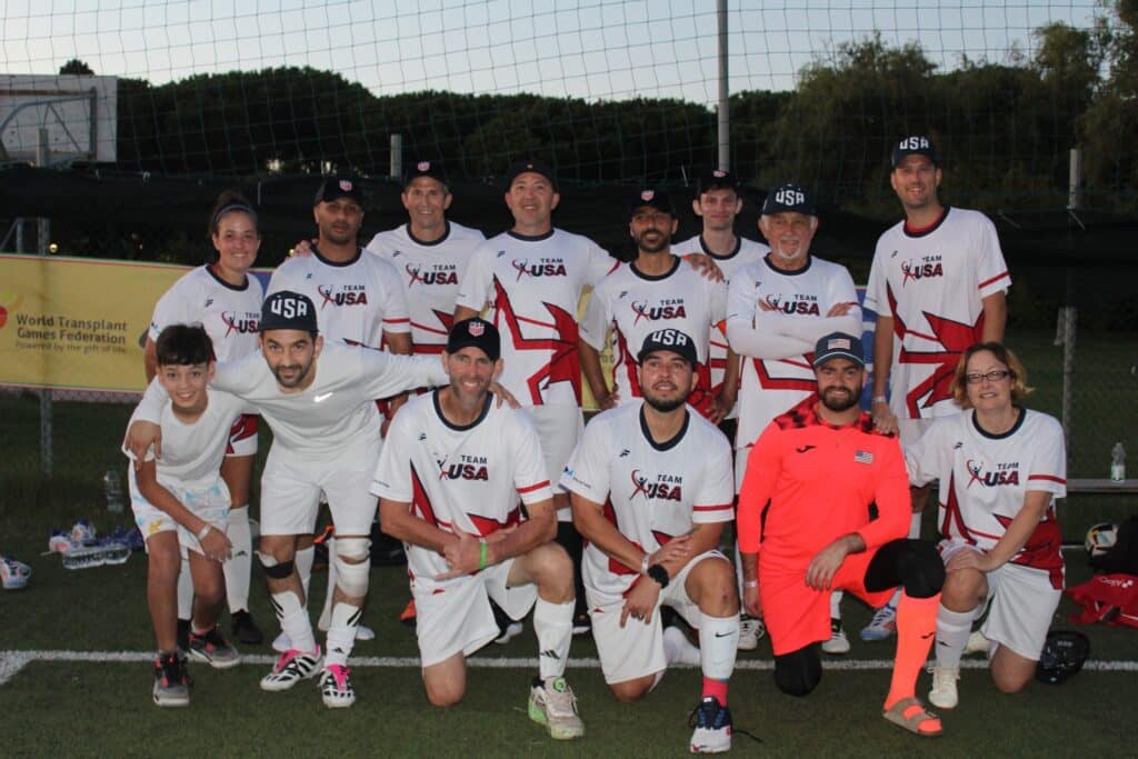 A group of players from a coed soccer team wearing white uniforms (except for the goalie in orange), posing for a team photo