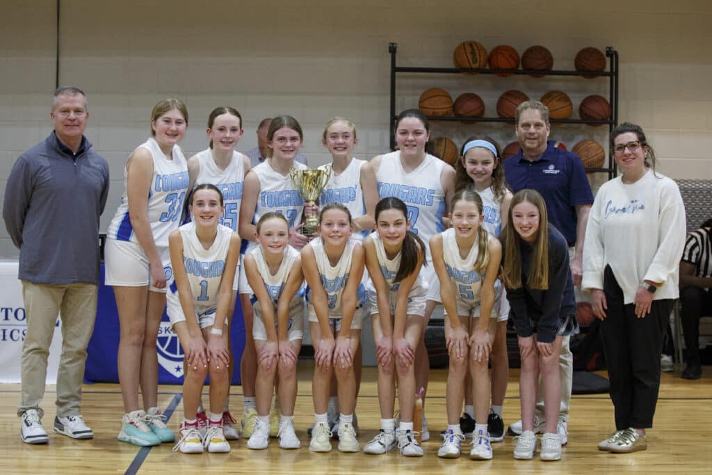 Middle school girls basketball team posing for a team photo on the court with coaches after a championship win