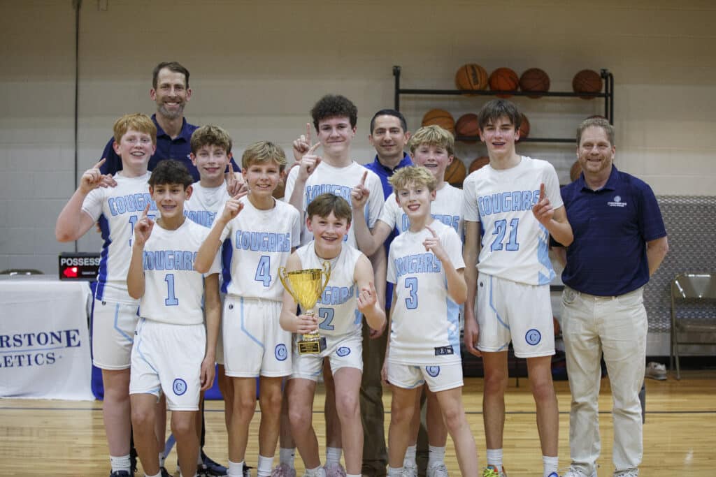 Middle school boys basketball team posing for team photo  on the court with coaches after a championship win.