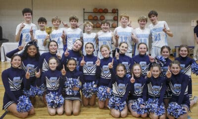 Middle school boys basketball team posing for team photo on the court with the school's cheerleaders.