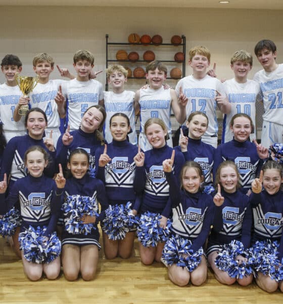 Middle school boys basketball team posing for team photo on the court with the school's cheerleaders.