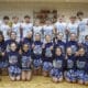 Middle school boys basketball team posing for team photo on the court with the school's cheerleaders.