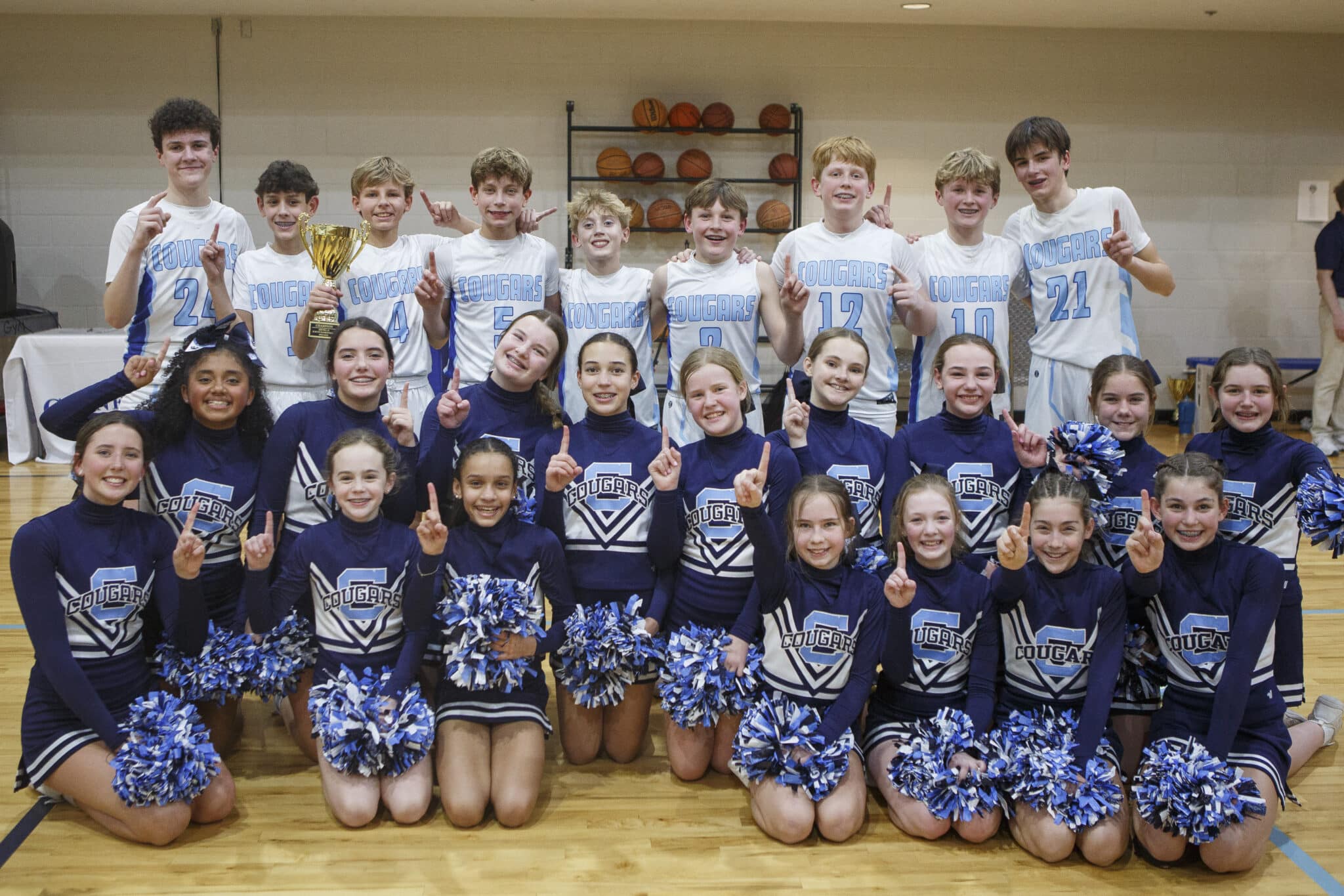 Middle school boys basketball team posing for team photo on the court with the school's cheerleaders.