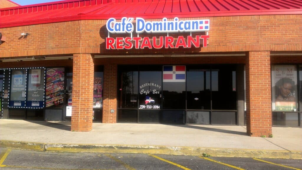 Exterior of Cafe Dominican restaurant in Norcross, GA. Brick, strip mall building with parking in front and restaurant signage above entrance