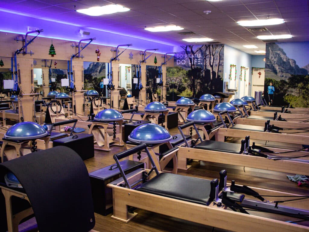 Interior of a pilates studio in Peachtree Corners, GA. The decor is brown, black and purple. There are rows of pilates machines along the each side of the room.