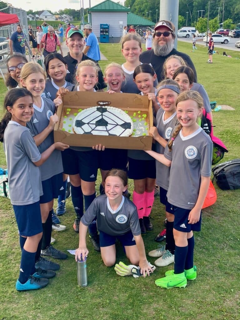 Youth soccer team with coaches holding up a giant cookie cake after a match