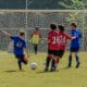 A group of kids, some in blue jerseys and some in red, playing soccer. Number 41 is kicking the ball towards the goal, where the other team's goalie waits.