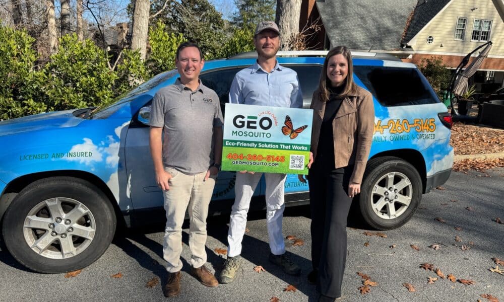 Two men and one woman standing next to a blue SUV with company logo on it and holding a sign for Geo Mosquito.