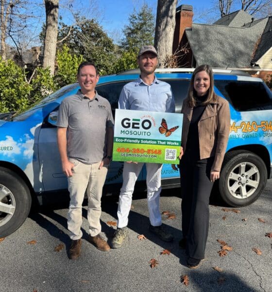 Two men and one woman standing next to a blue SUV with company logo on it and holding a sign for Geo Mosquito.