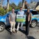 Two men and one woman standing next to a blue SUV with company logo on it and holding a sign for Geo Mosquito.