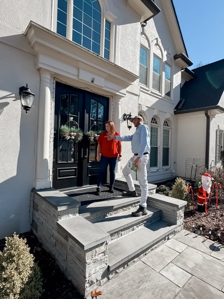 A pest control technician from Geo Mosquito talks to a woman wearing a red top and black pants on the steps leading up to her home's front door.