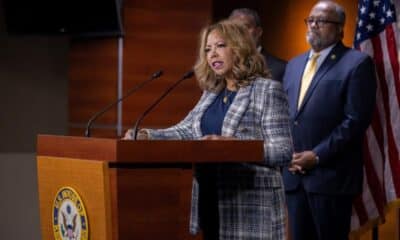 Rep. McBath, of Georgia's 6th District, at a podium speaking to an audience. A man and woman stand behind her, along with an American flag.